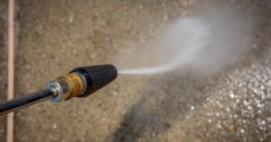 Concentrated water jet from a pressure washer nozzle striking a concrete surface